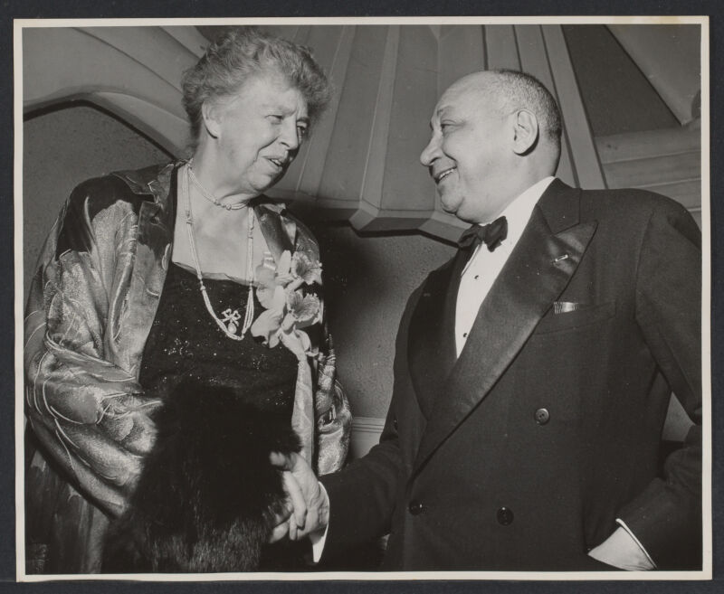 Eleanor Roosevelt (left) and Louis T Wright (right) in evening clothes shaking hands.