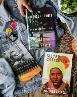 Three Penguin Random House books spread across a denim jacket: The Purpose of Power, The Fire Next Time, and Sister Outsider