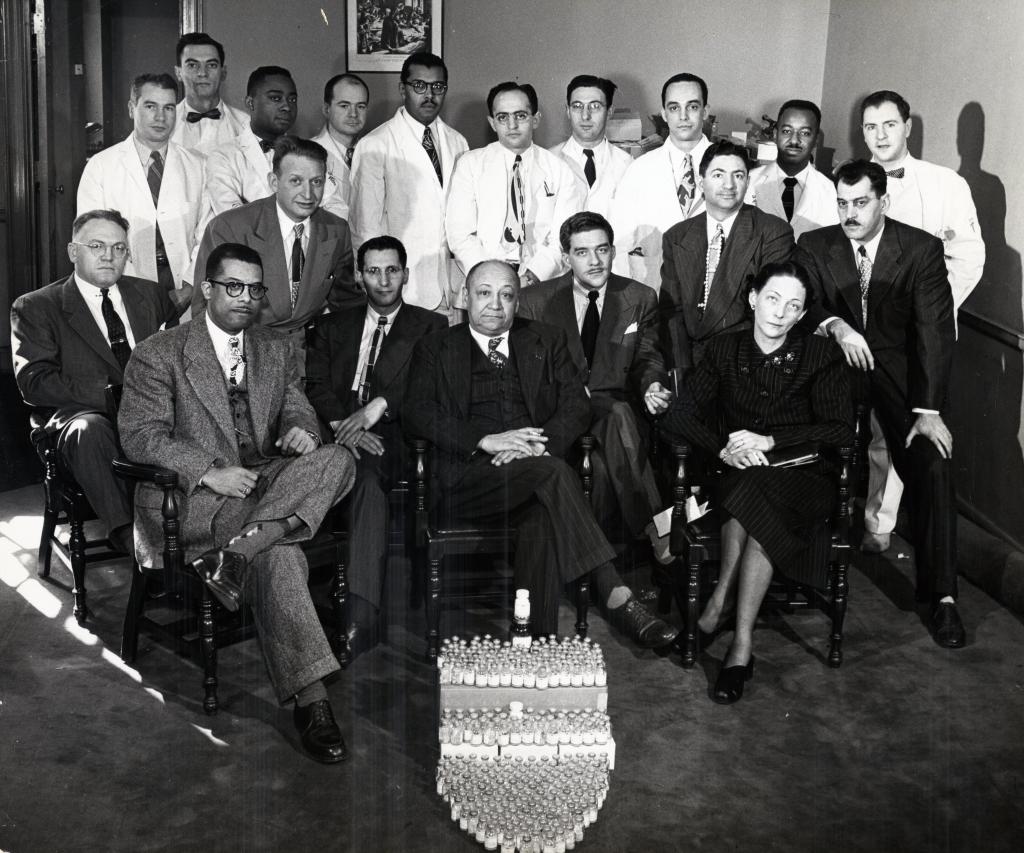 Myra Logan with Louis Tompkins Wright and other members of the Aureomycin research group behind a display of vials at Harlem Hospital in 1949