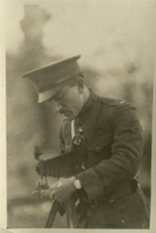 Levine in uniform with a cap and moustache bending slightly over a camera on a tripod.