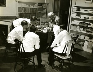 Dickinson sitting with a group of students in lab coats studying a mold.