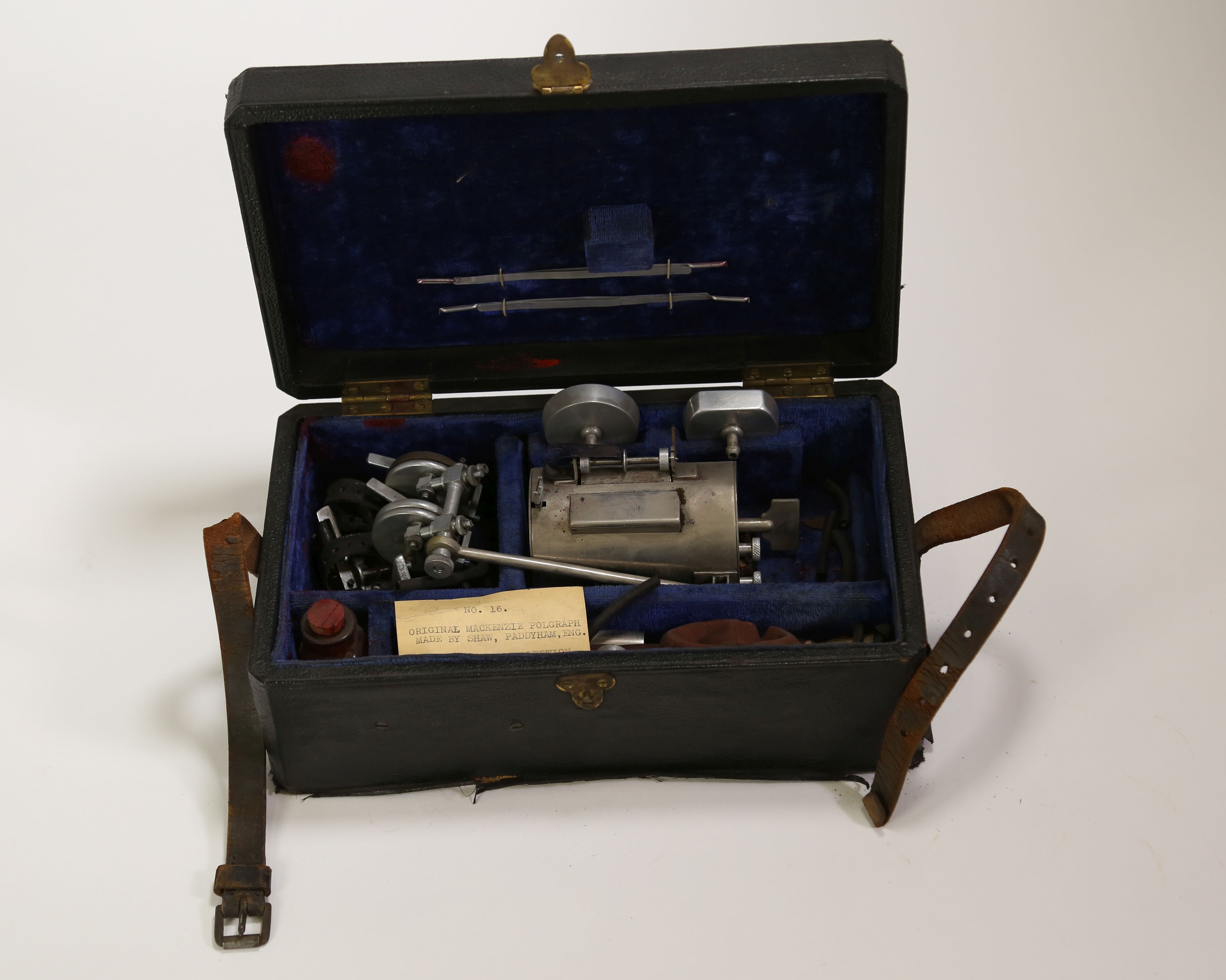 Disassembled Mackenzie Polygraph machine. The case containing the object is open to show the parts of the object, which are not assembled.