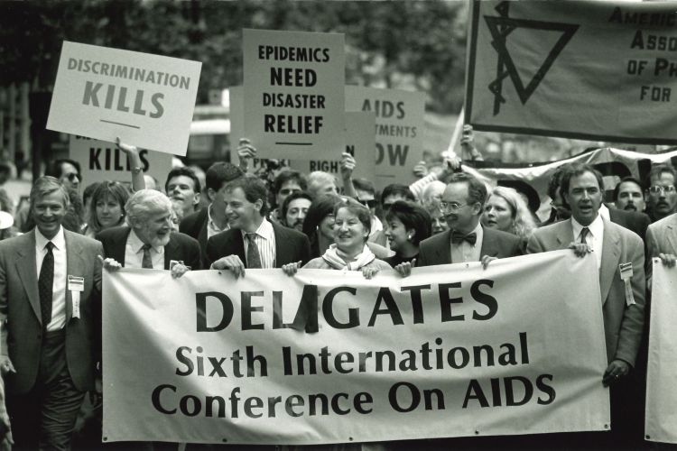 Demonstrators march carrying signs that read Deligates 6th International Conference on AIDS; Discrimination kills; and Epidemics need disaster relief.