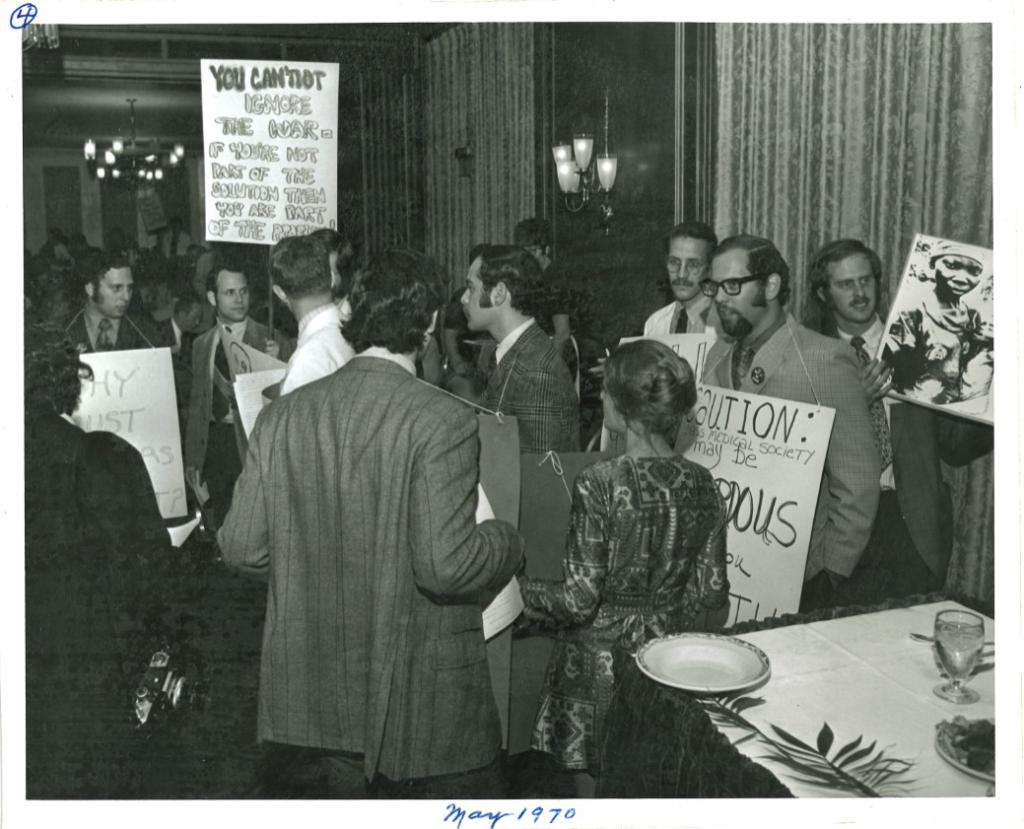 People in suits hold protest signs in a hotel hallway.