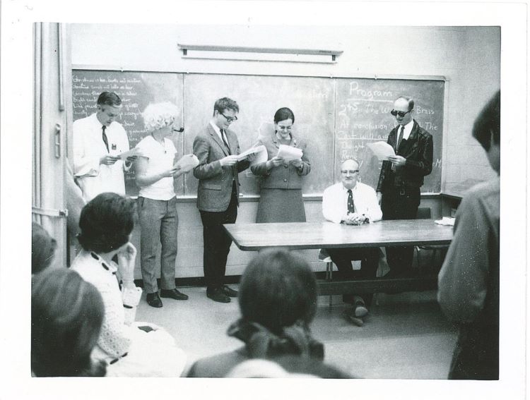 People reading from scripts at the front of a classroom.