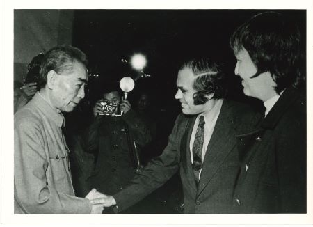 Zhou Enlai and Victor Sidel shake hands while photographers take pictures of them.