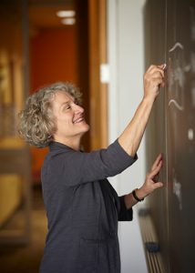 Nancy Kane smiling and writing on a chalkboard.