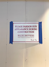 Sign taped to the wall reading "Please pardon our appearance during construction."