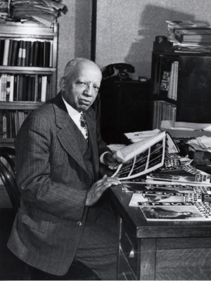 Black and white photo of Carter G. Woodson seated at a desk.