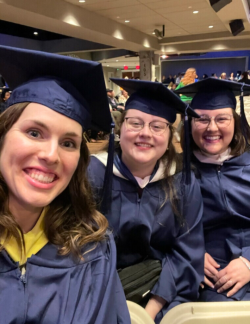 Photo of three female graduates smiling in dark blue regalia.