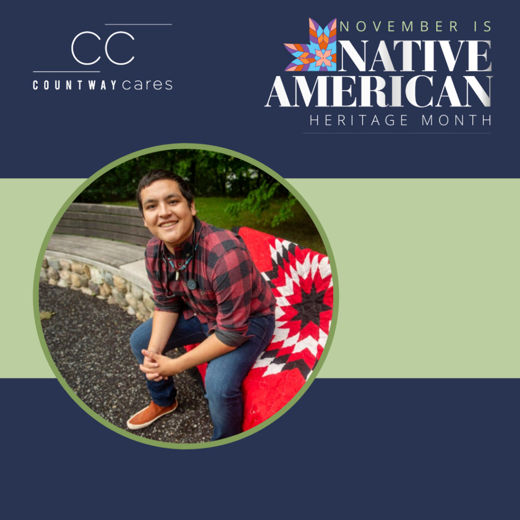 On a navy blue background: white Countway Cares icon in top left corner, colorful flower image with "November is Native American Heritage Month" written in top right corner. In the center there is a green horizontal bar and a green circle with a photo of Victor Lopez-Carmen seated outside on a vibrant red, black, and white blanket.