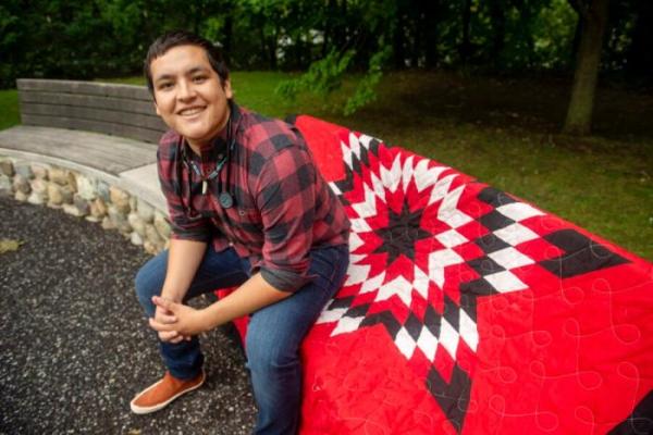 Victor Lopez-Carmen seated outside on a vibrant red, black, and white blanket.