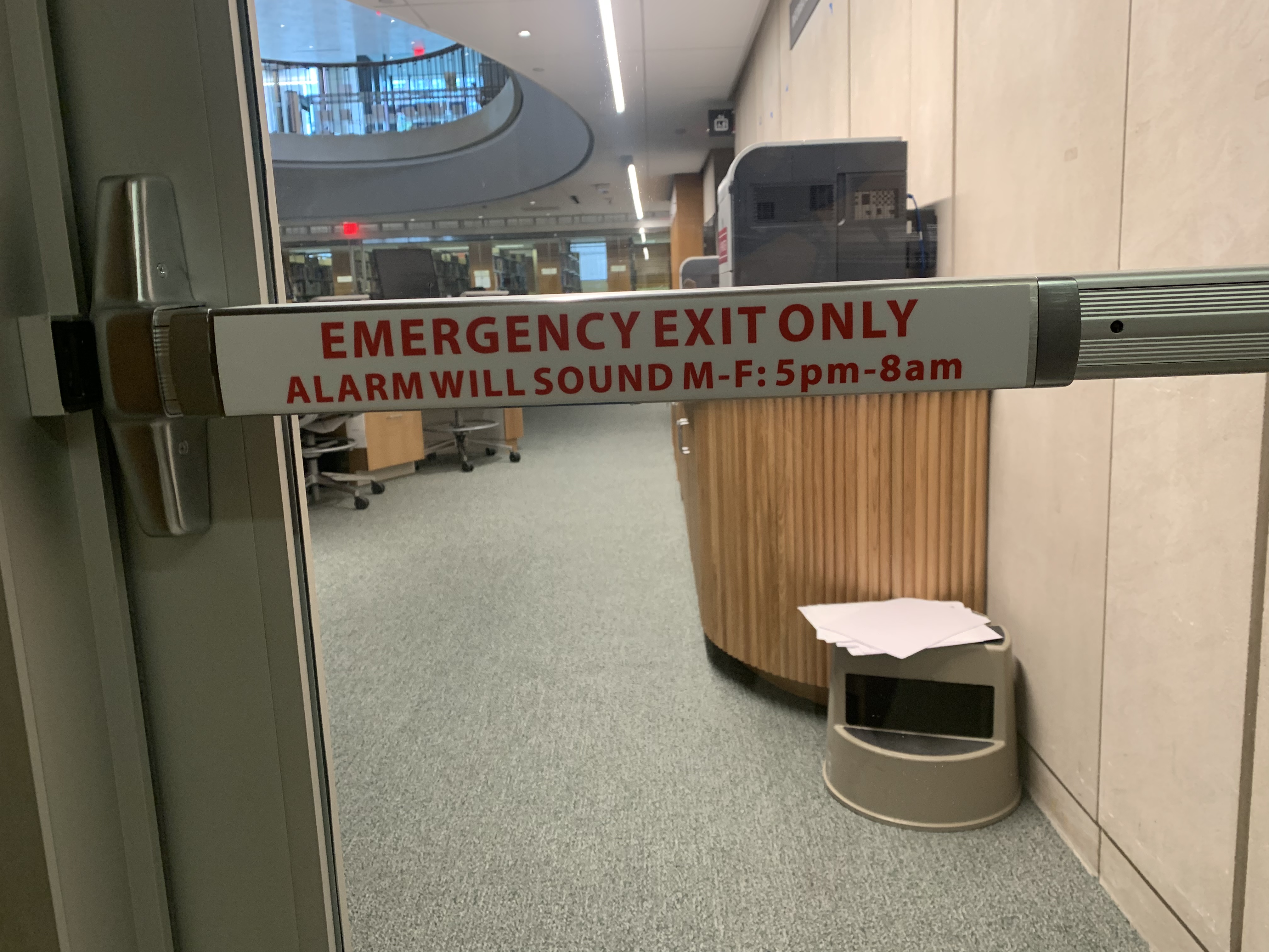 Sign on an interior glass door that says: Emergency exit only. Alarm will sound Monday to Friday from 5 p.m. to 8 a.m.