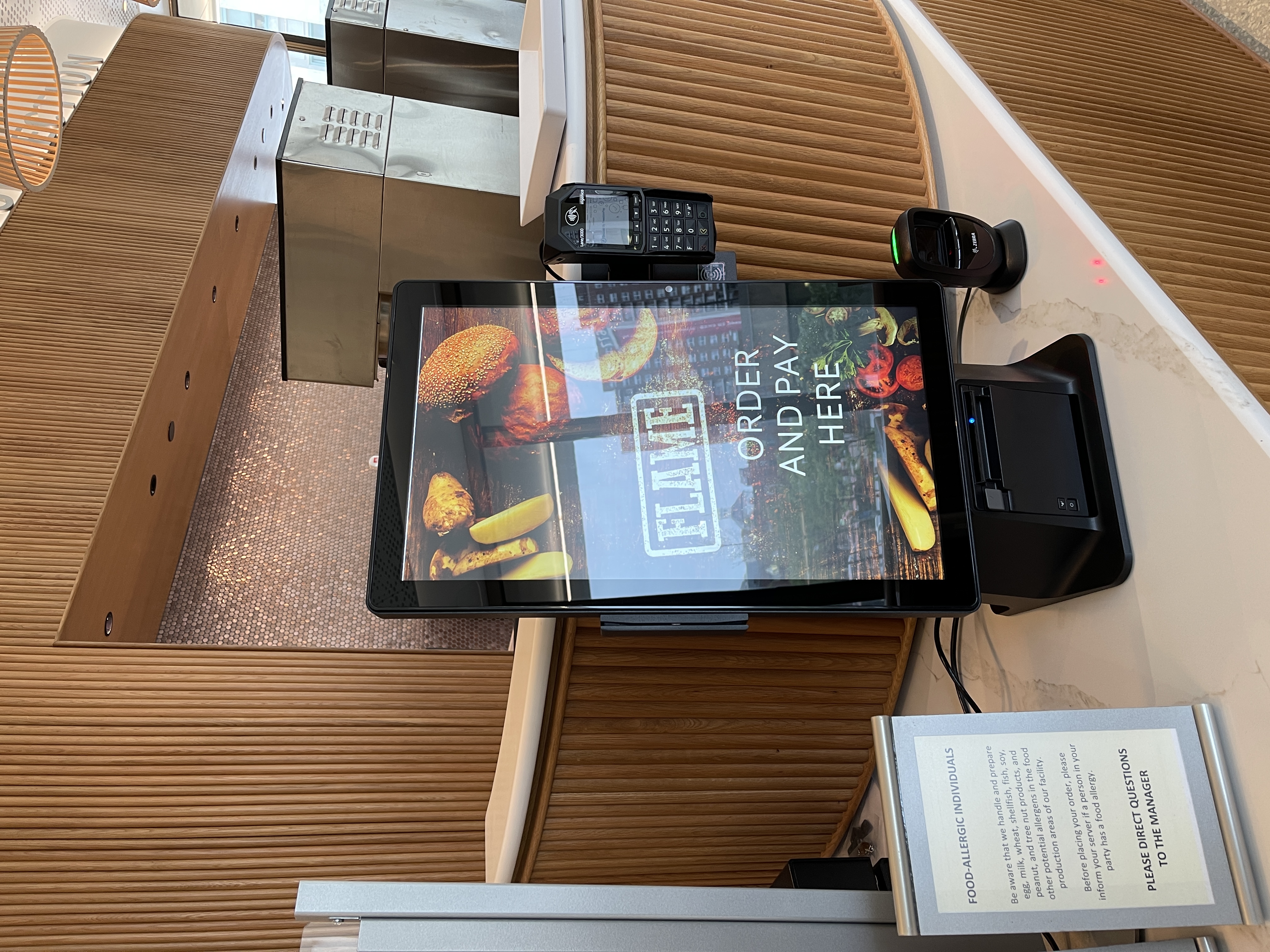 touch-screen point-of-sale system in the café. The screen says Flame - order and pay here. There is a card reader on the right-hand side.