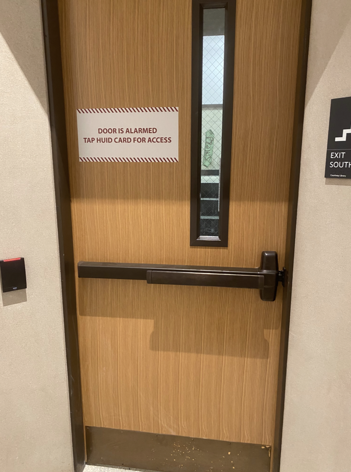 Emergency exit door with a sign that says door is alarmed; tap HUID card for access.