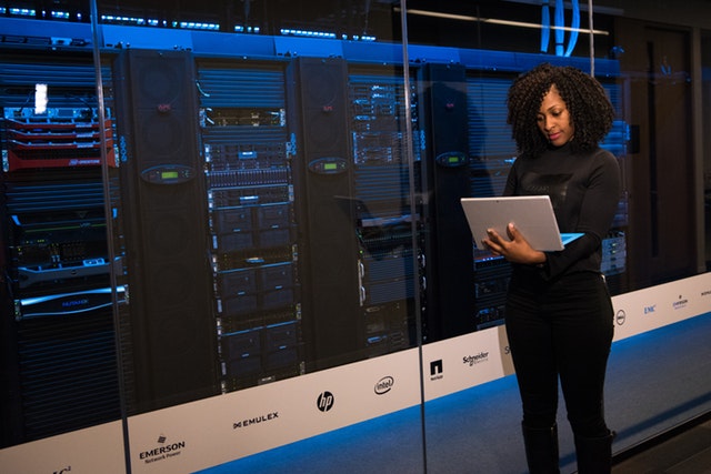 Women holding a computer standing in front of computer servers