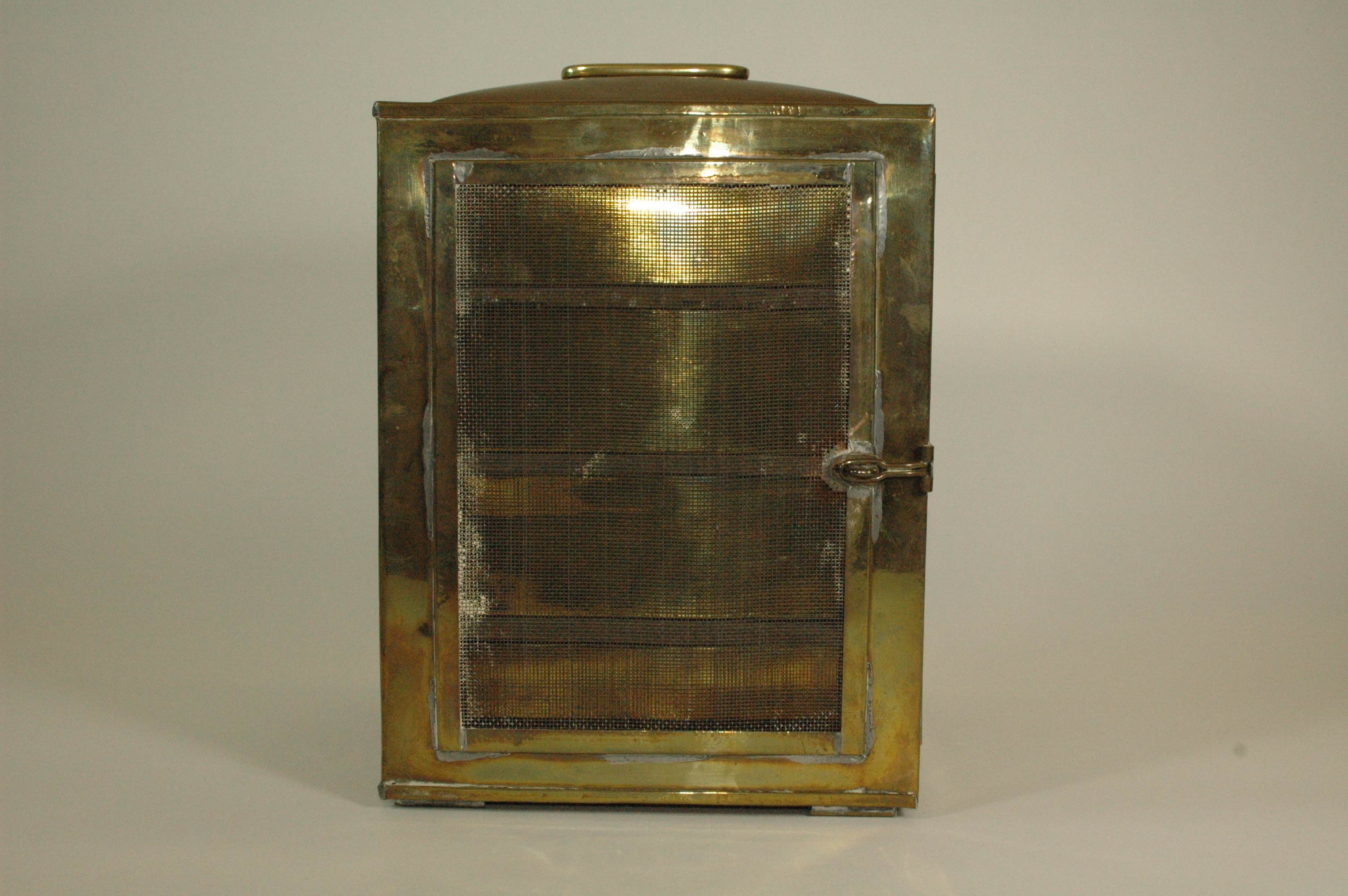Rectangular tabletop sterilizer with mesh side panels. Brass body with handle on top. One door on front of unit with latch. Door opens to reveal four brass drawers, empty.