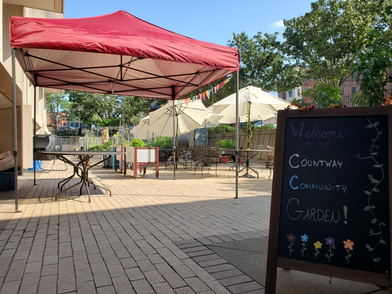 A tent set up in the Countway Community Garden next to a chalkboard sign that reads: Welcome to the Countway Community Garden.