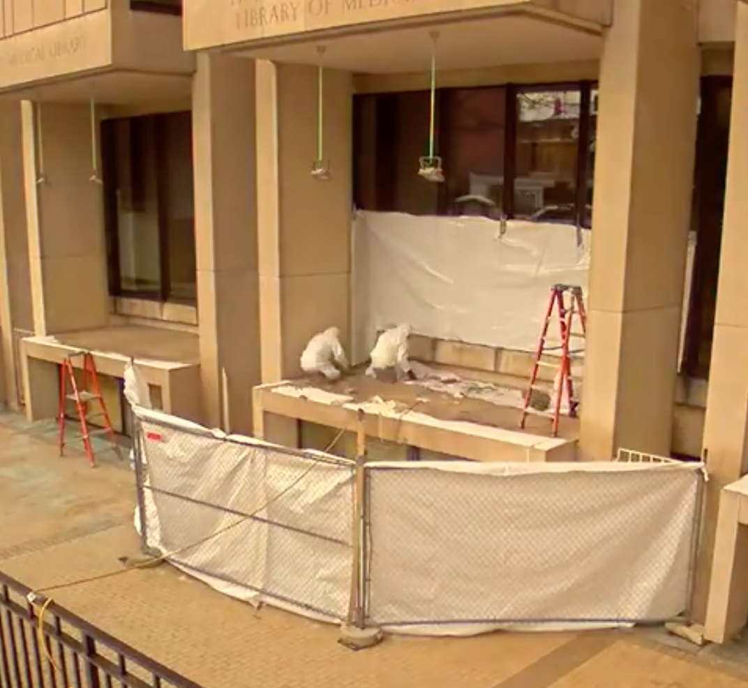 outside fenced portion of the library with three construction men wearing white clothes.