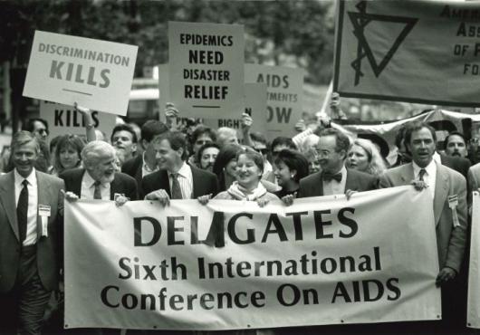 Demonstrators march carrying signs that read Deligates 6th International Conference on AIDS; Discrimination kills; and Epidemics need disaster relief.
