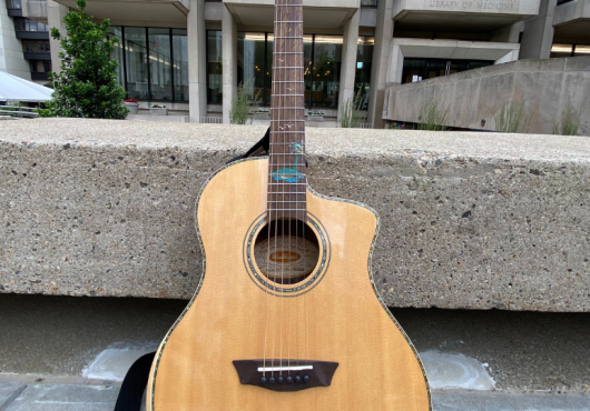 Photo of an acoustic guitar propped against a stone bench in front of Countway Library