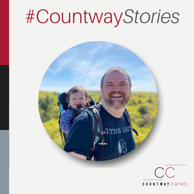 Photograph of Keith Pierce smiling outdoors with a baby on his back in a hiking baby carrier under the text #CountwayStories