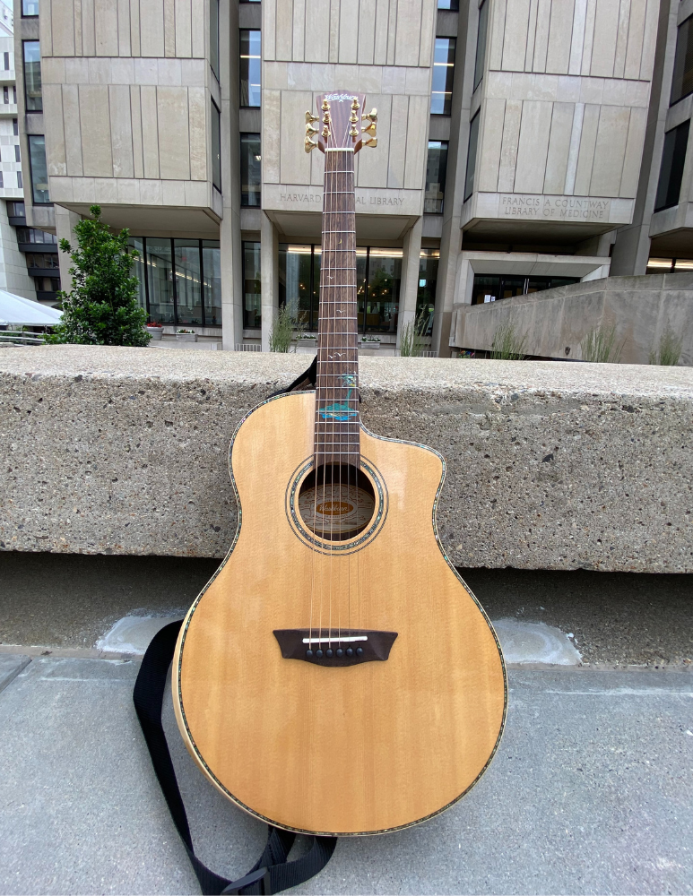 Photo of an acoustic guitar propped against a stone bench in front of Countway Library